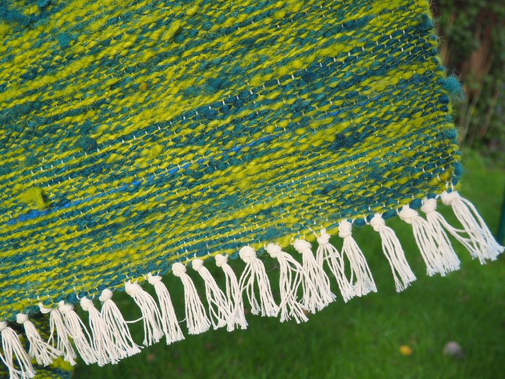 Ecke eines gewebten grünblauen Teppichs mit weißen Fransen
